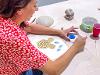 Over-the-shoulder view of a smiling instructor using colored glaze to paint yellow flowers and blue leaves.