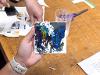 Hand holding a small canvas. On the canvas is an incomplete image of a multicolored butterfly.