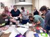 Instructors crowd around a table and watch as Kendra Cremin soaks a small magazine clipping in a liquid solution.