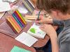 Over-the-shoulder view of an instructor using a blue colored pencil to add hue to a drawing of a flower in a journal.