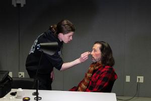 Student applying special effects makeup to actor.