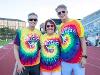 Wichita State President Rick Muma, retired executive vice president and provost Shirley Lefever, and First Gentleman Rick Case stand on a stadium track wearing matching rainbow tie-dye “Clash of the Colleges” shirts. All three are smiling and wearing sunglasses.