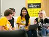 A group of students sit together with laptops and notebooks in a collaborative workspace branded “WiDGET.