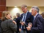 First Gentleman Rick Case and Wichita State President Rick Muma hold drinks and chat with a woman during a memorial service reception. Other guests mingle in the background.