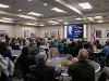 A large group of Wichita State University faculty and staff sit at round tables, facing a podium and large screen during a welcome reception for Dr. Monica Lounsbery, senior executive vice president and provost. A slide featuring her photo and biography is displayed on the screen at the front of the room.