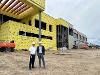 John Tomblin and President Rick Muma stand in front of the under-construction Hub for Advanced Manufacturing and Research, wearing hard hats and safety gear at the Innovation Campus site.