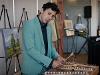 A person wearing a green suit plays a mallet percussion instrument at the Ulrich50 Gala. Behind them, several colorful paintings are displayed on easels.