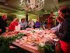 Guests gather around a table of food to fill their plates. On the table is a variety of fruits, vegetables and other snacks.