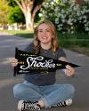 A student seated cross-legged holds a Shocker pennant.