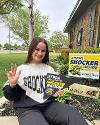 A student sits outside their home beside their Future Shocker yard sign.