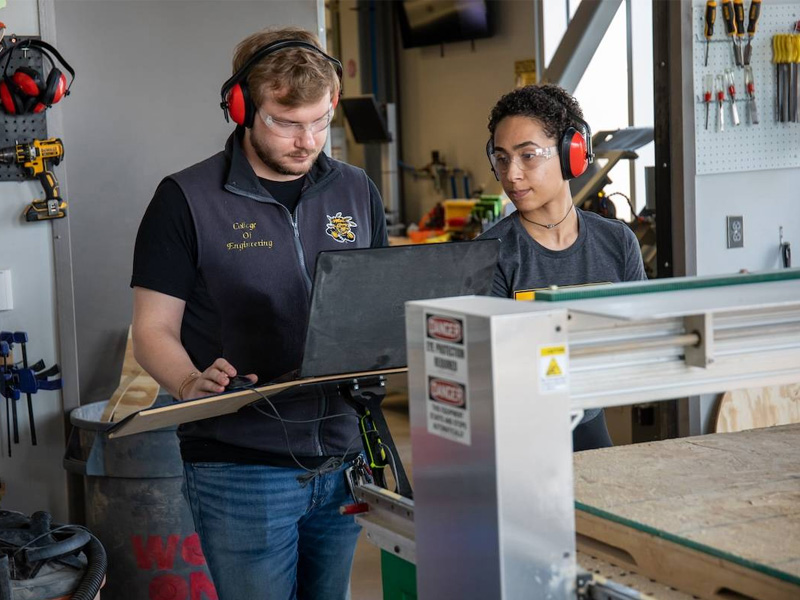 Students working in a laboratory wearing safety glasses, protective hearing and working on machinery.