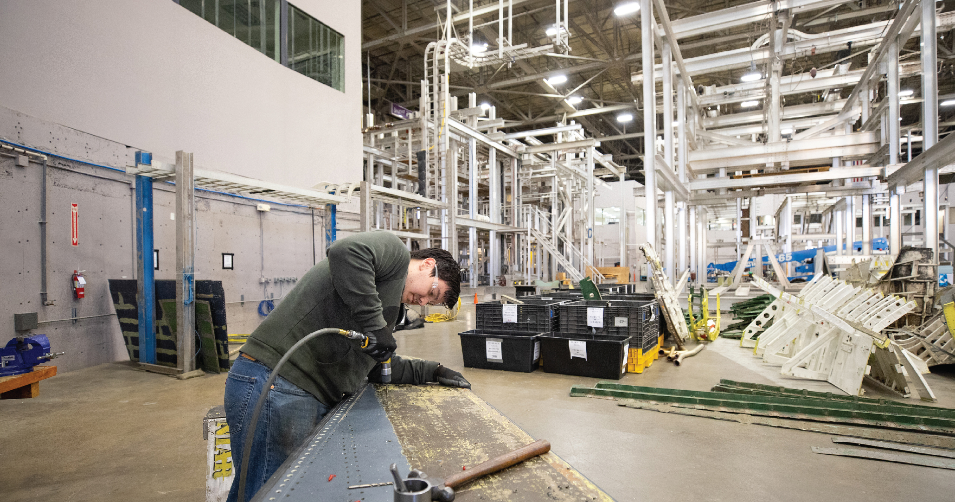 Employee working on a stripped down airplane wing on a workbench with a riveter.
