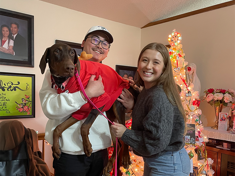 Photo of Peter Vu and one other. Peter is holding a dog that is wearing a red sweater