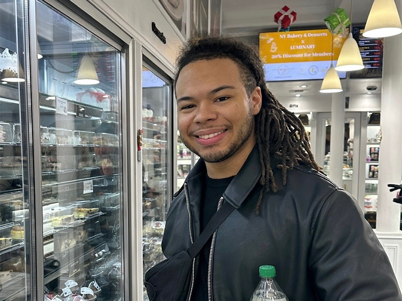 Photo of Cameron Davis in a bakery, holding pizza boxes.