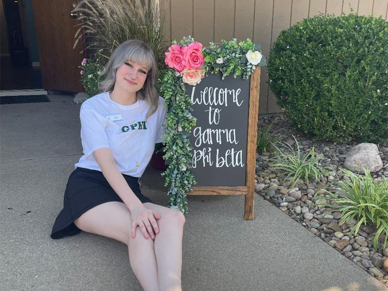 Photo of Emily Evans in front of a Gamma Phi Beta welcome sign