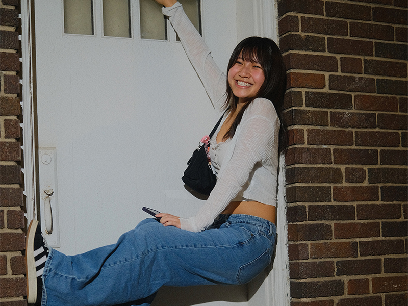 Photo of Christine Nguyen hanging from an old white door frame in a brick wall.