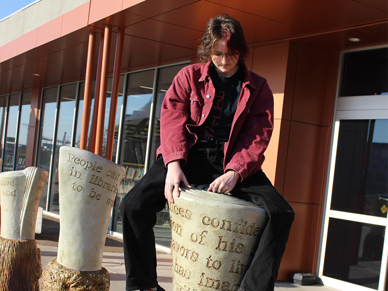 Photo of Rohan Spillman sitting on top of a pillar in front of the Wichita Public Library.