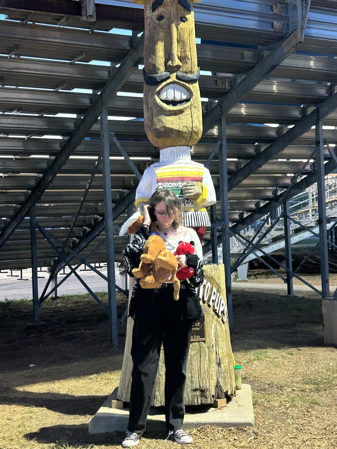 Photo of Rohan Spillman in front of a wooden statue holding two stuffed animals.
