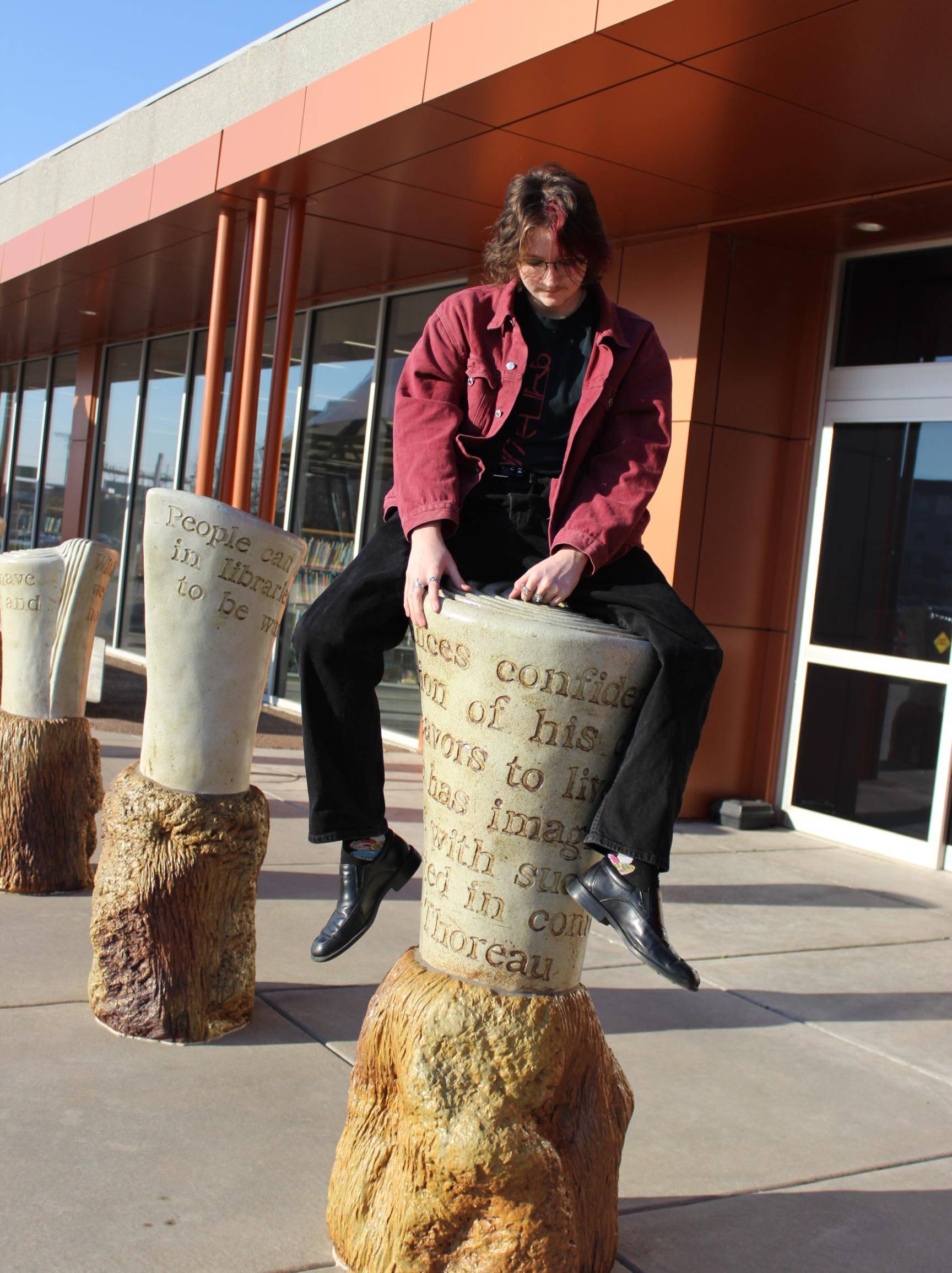 Photo of Rohan Spillman sitting on top of a pillar in front of the Wichita Public Library.