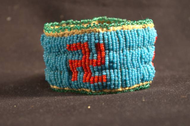 A rawhide bracelet that is decorated primarily with blue beads and swastikas made from red beads.