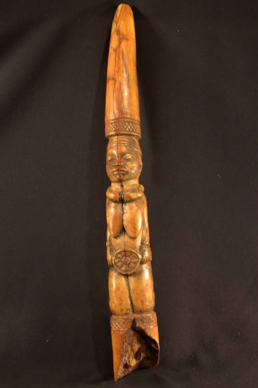 ange-colored tusk with kneeling female figure wearing a necklace and holding a disk in front. 