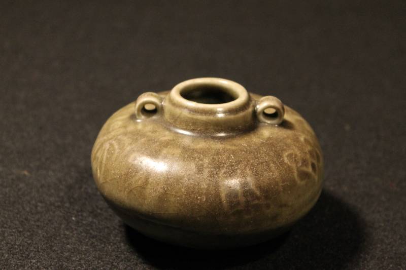 Medium size jarlet glazed with a dark green Celadon, finished with two lug handles at the shoulder. Geometric and organic shapes form decoration on body of vessel.