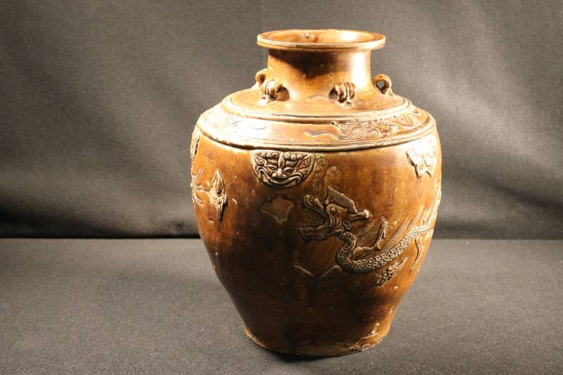 Large, rust-brown, classically shaped storage jar with a large-headed dragon flying horizontally through clouds circumventing the outside walls of the jar.