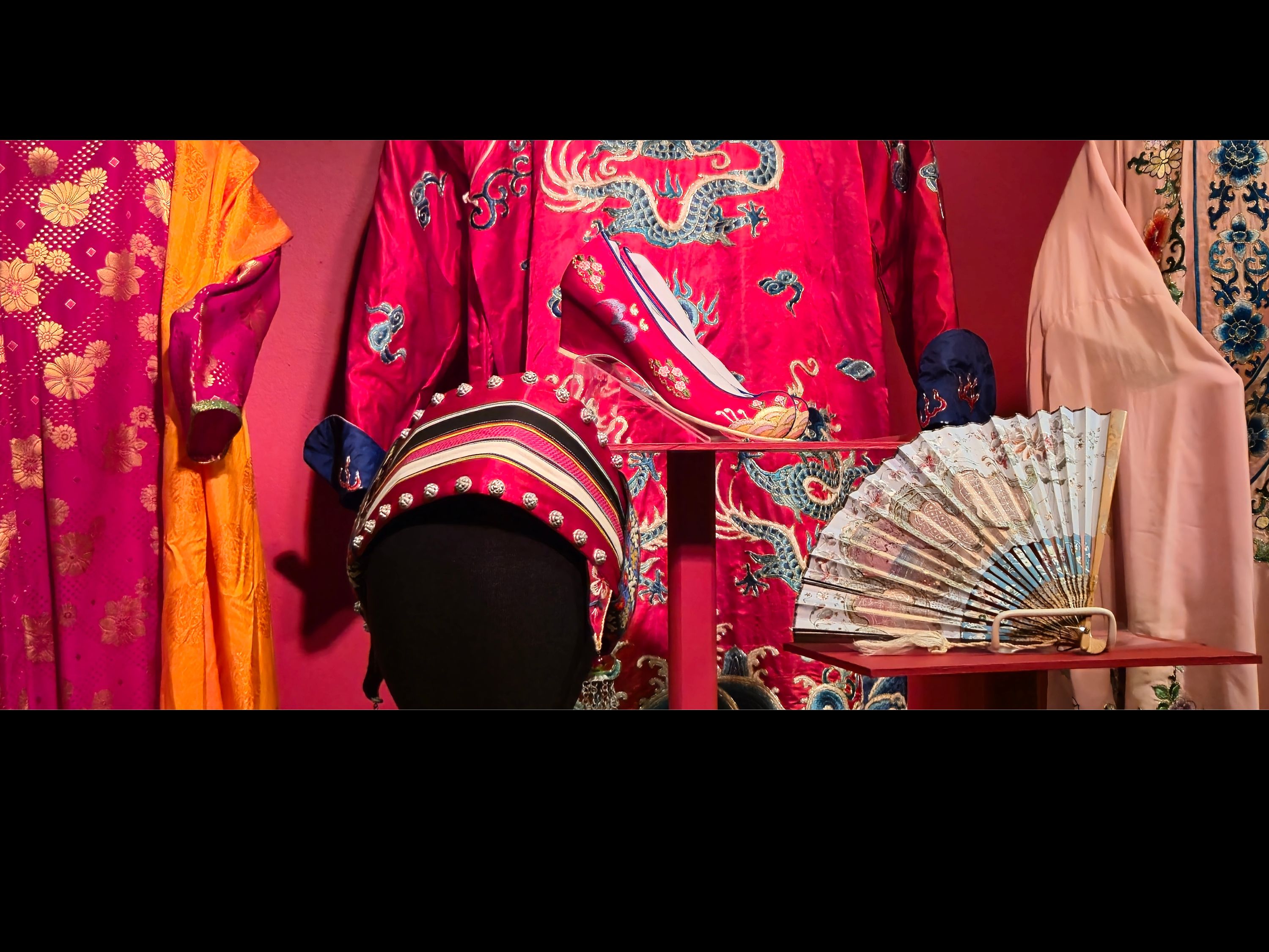 Open case with red background with mannequins and pedestals with garments on them. 