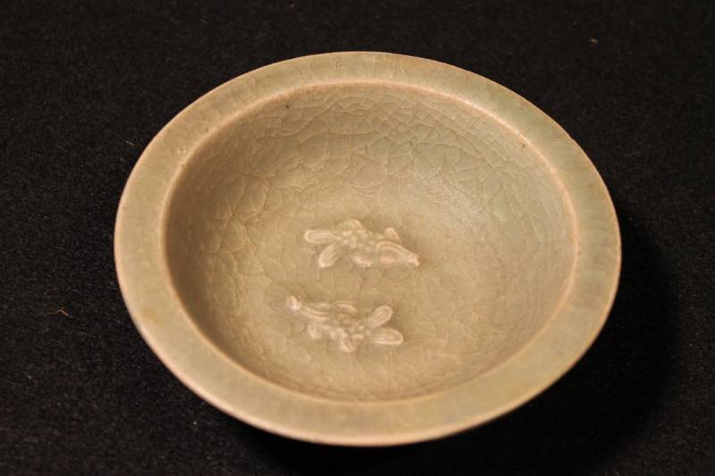 Small serving dish decorated with twin fish arranged in a ying-yang position in the center bottom of the bowl. The dish has a wide, flat lip, glazed dark green.