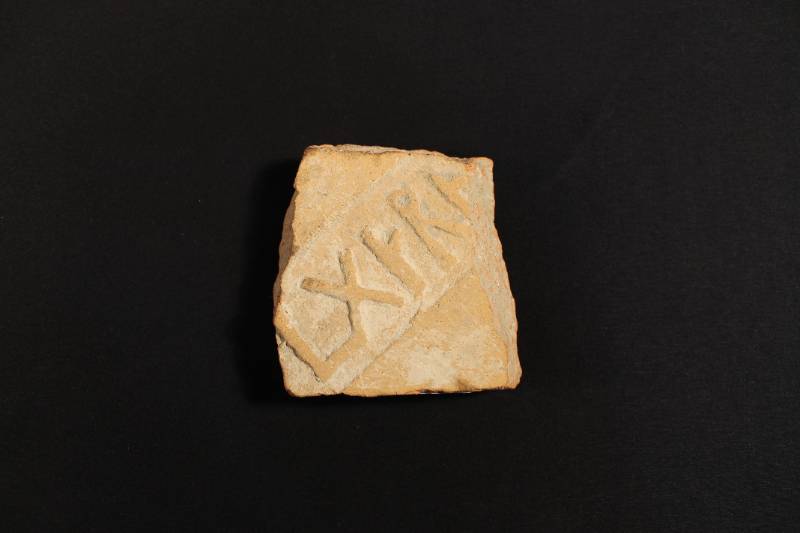The color of the tile is light tan. It has Greek writing or numerals carved into it.