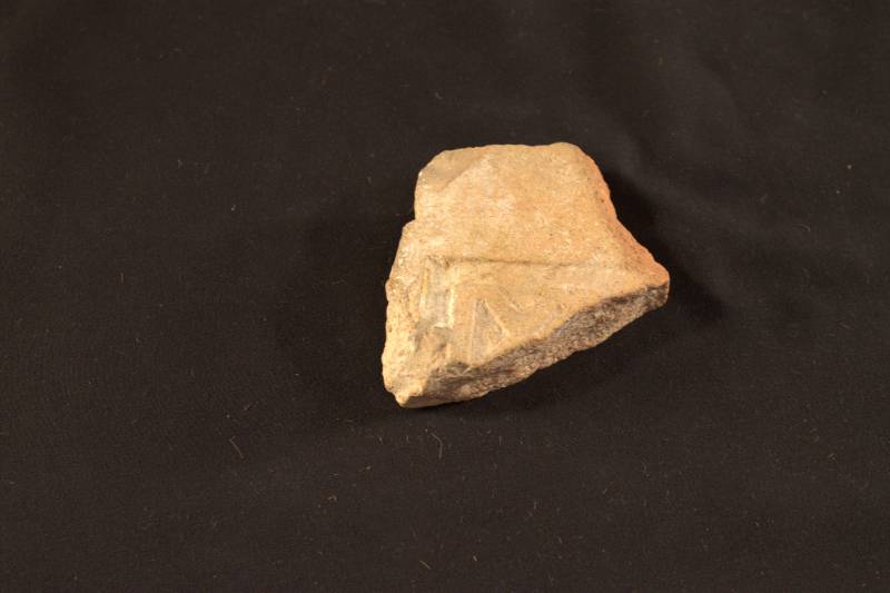 The tile is light tan in color. It has some Greek writing or numerals carved into it.