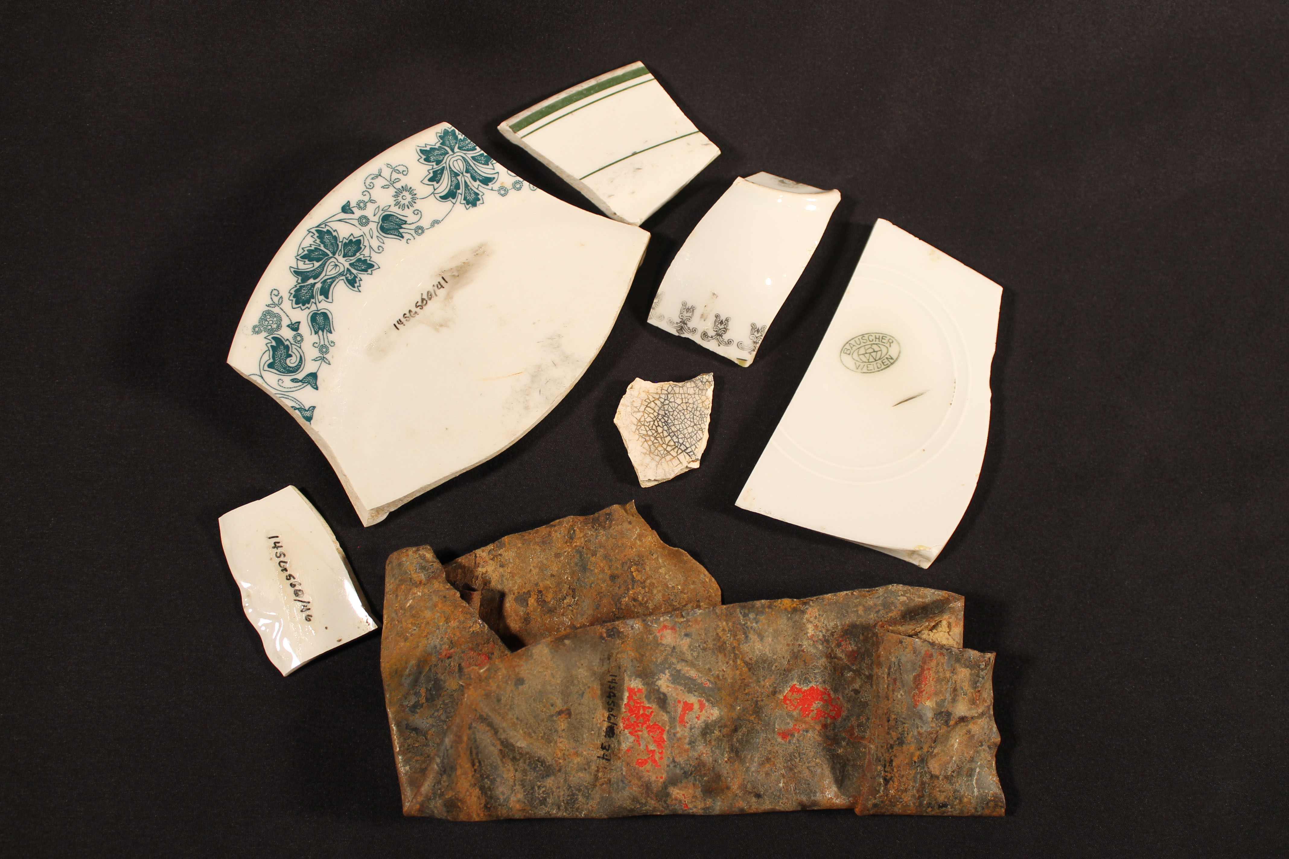Six broken pieces of white pottery that have blue accents. One large piece has a flower pattern along the rim. The tin can is red, but it's corroded and smashed.