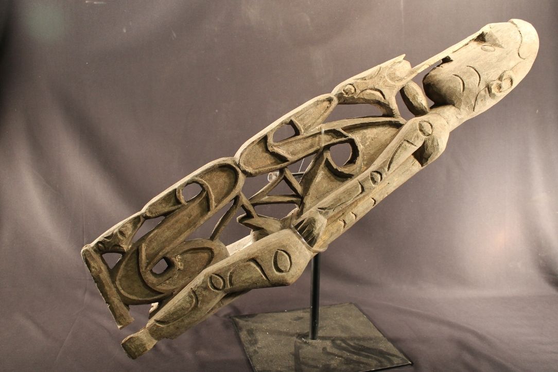 Carved male figure with broken off ankles. He has the tail of a Cuscus, a marsupial, wrapped around his torso and legs. A bird head is resting on him with its beak at the man’s neck. Moon and “c” shaped designs are also found on carvings.