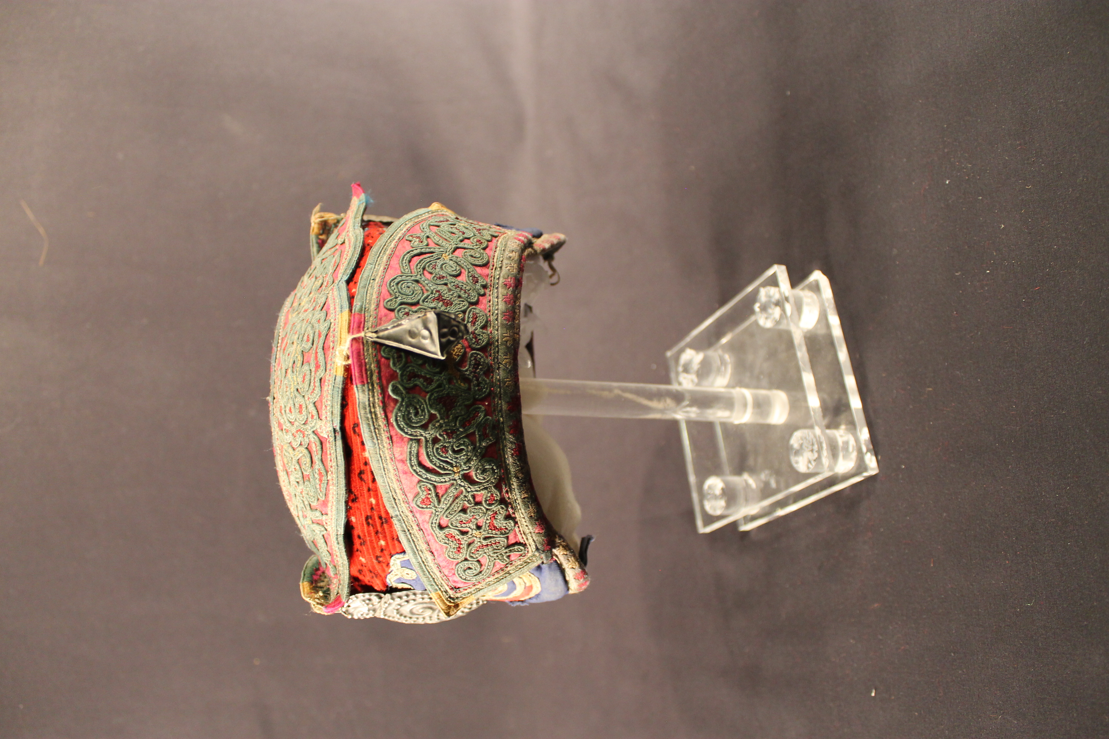 Multi-colored hat with spiral and flowing designs with three metal fish ornaments.