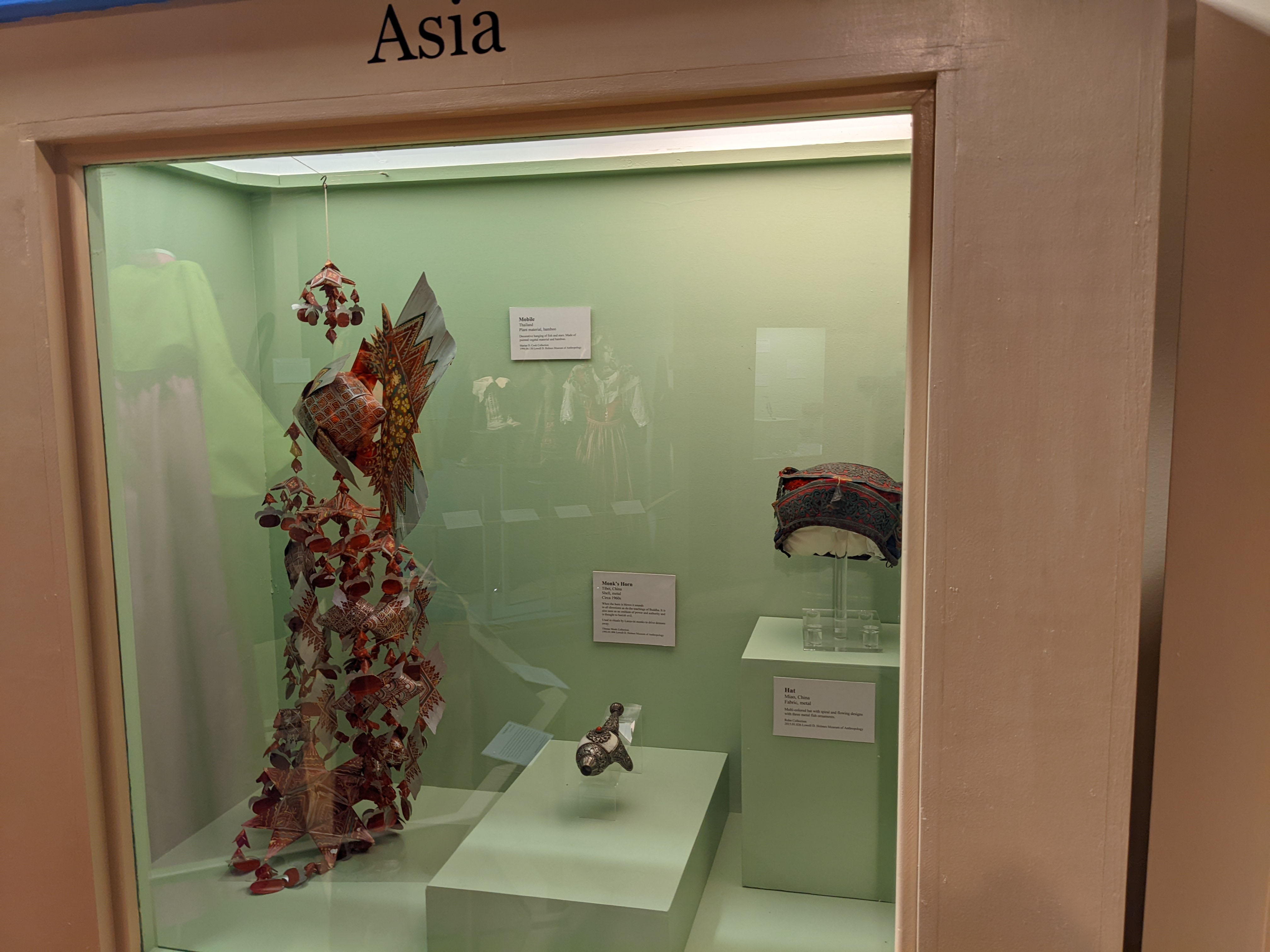 Green case with mobile, horn, and hat on display. Labels attached to the back wall on the exhibit
