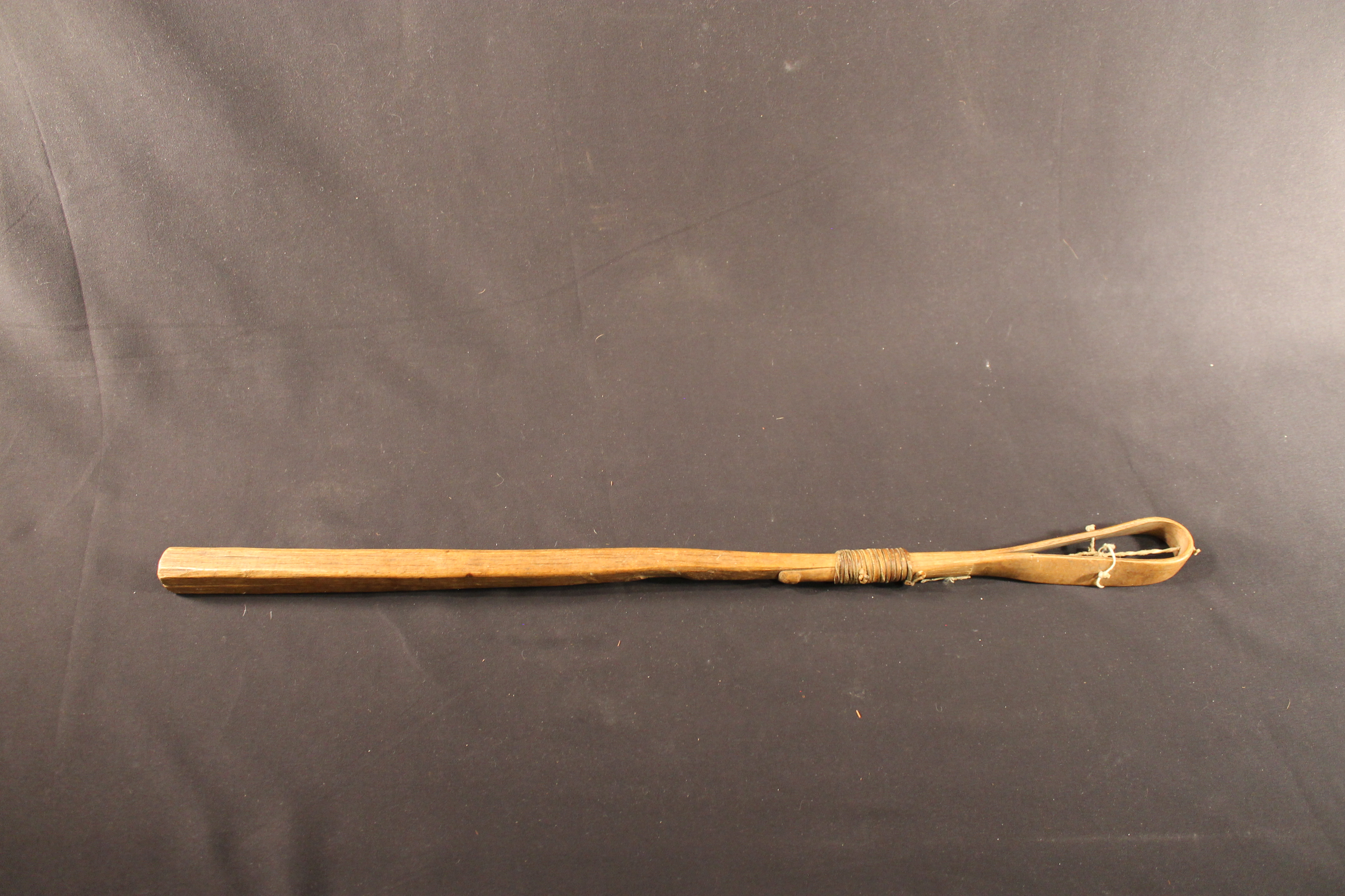 Lacrosse stick made of wood that has been bent into a loop at one end with a leather net in the center.