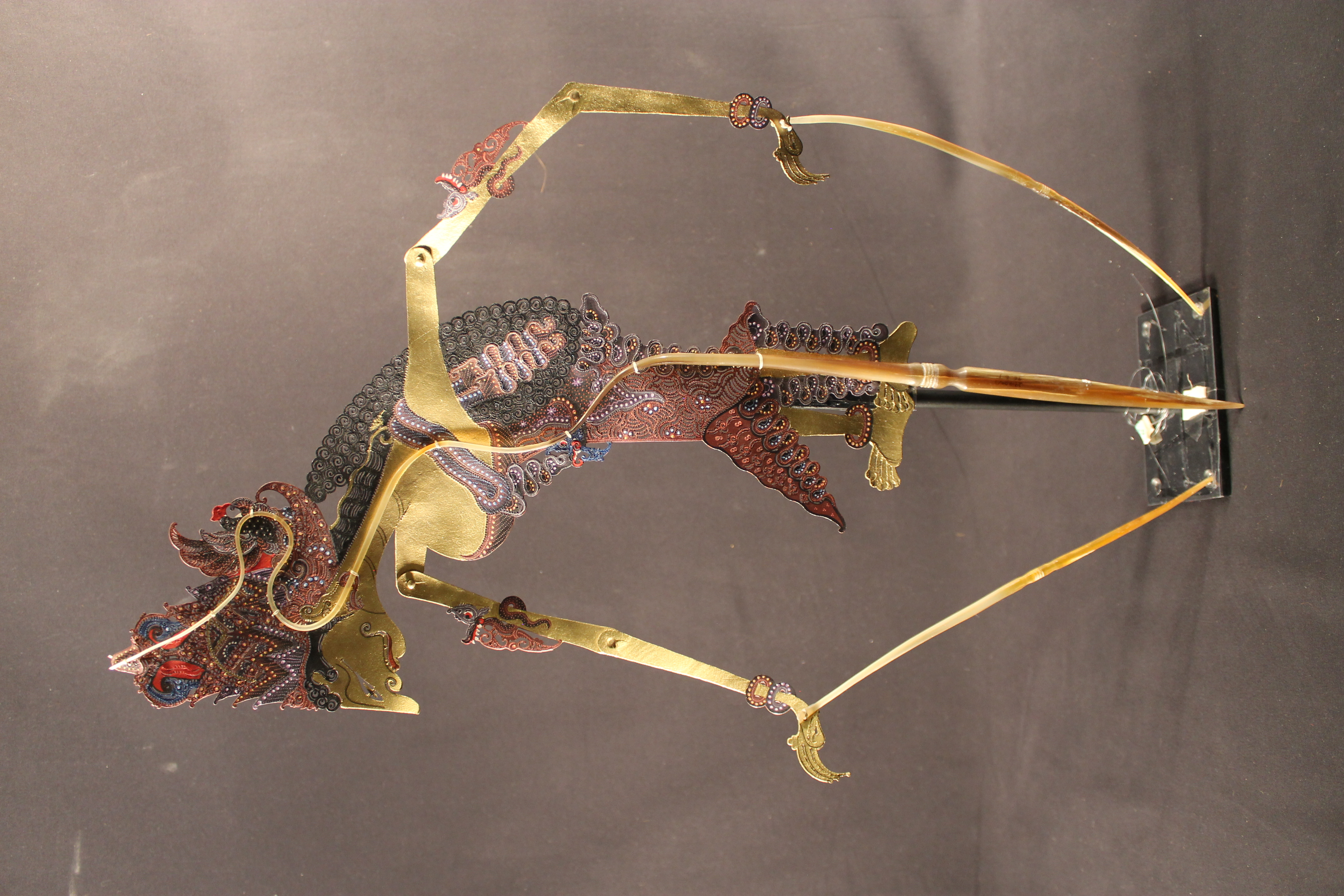 Paper puppet of a woman with long braided hair and wearing a red dress. The puppet has elongated arms attached to sticks that can move the puppet.