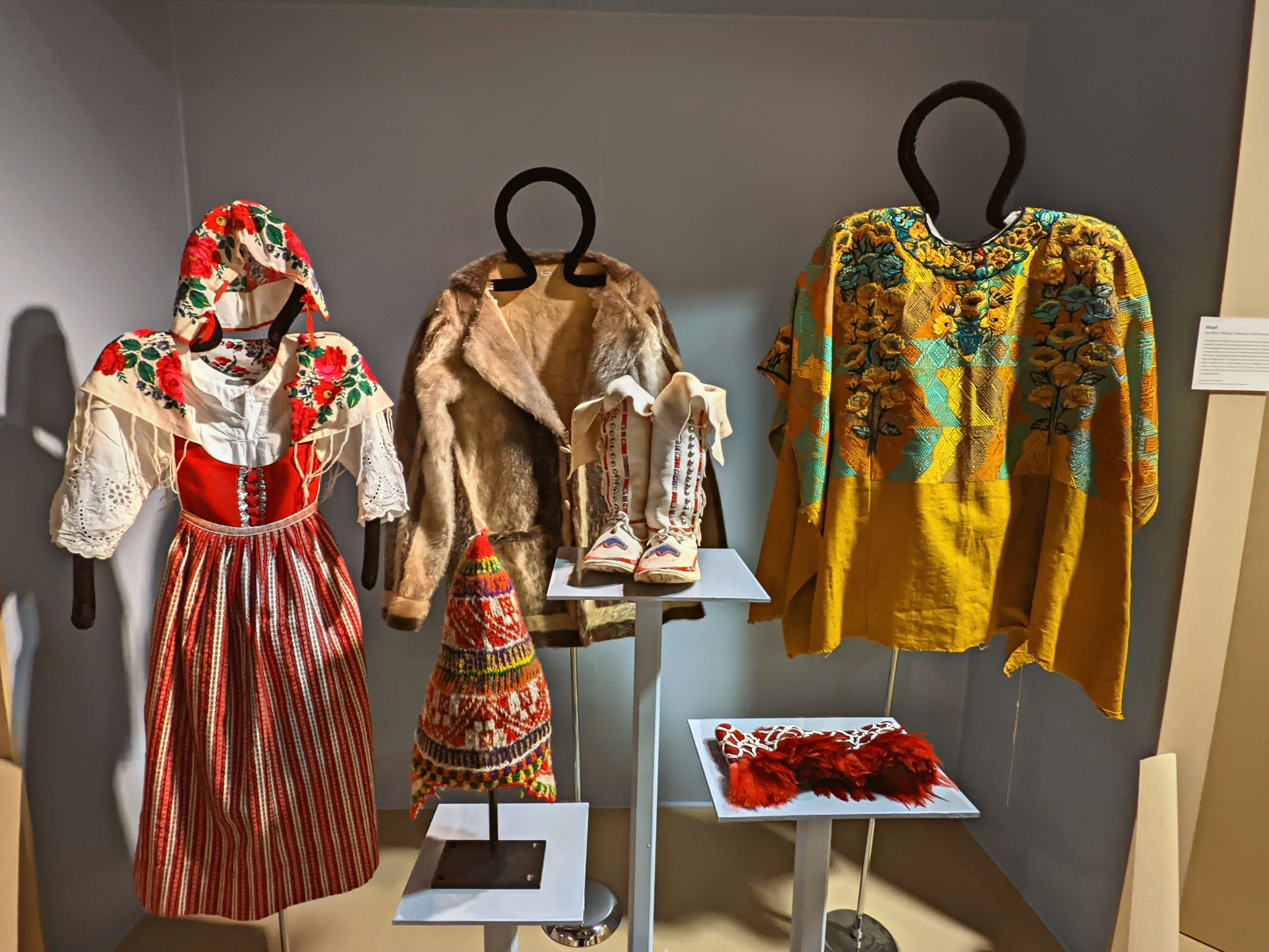 Open case with blue background with mannequins and pedestals with garments on them. The labels are attached to the side of the case and a rail that sits on the front of the display.