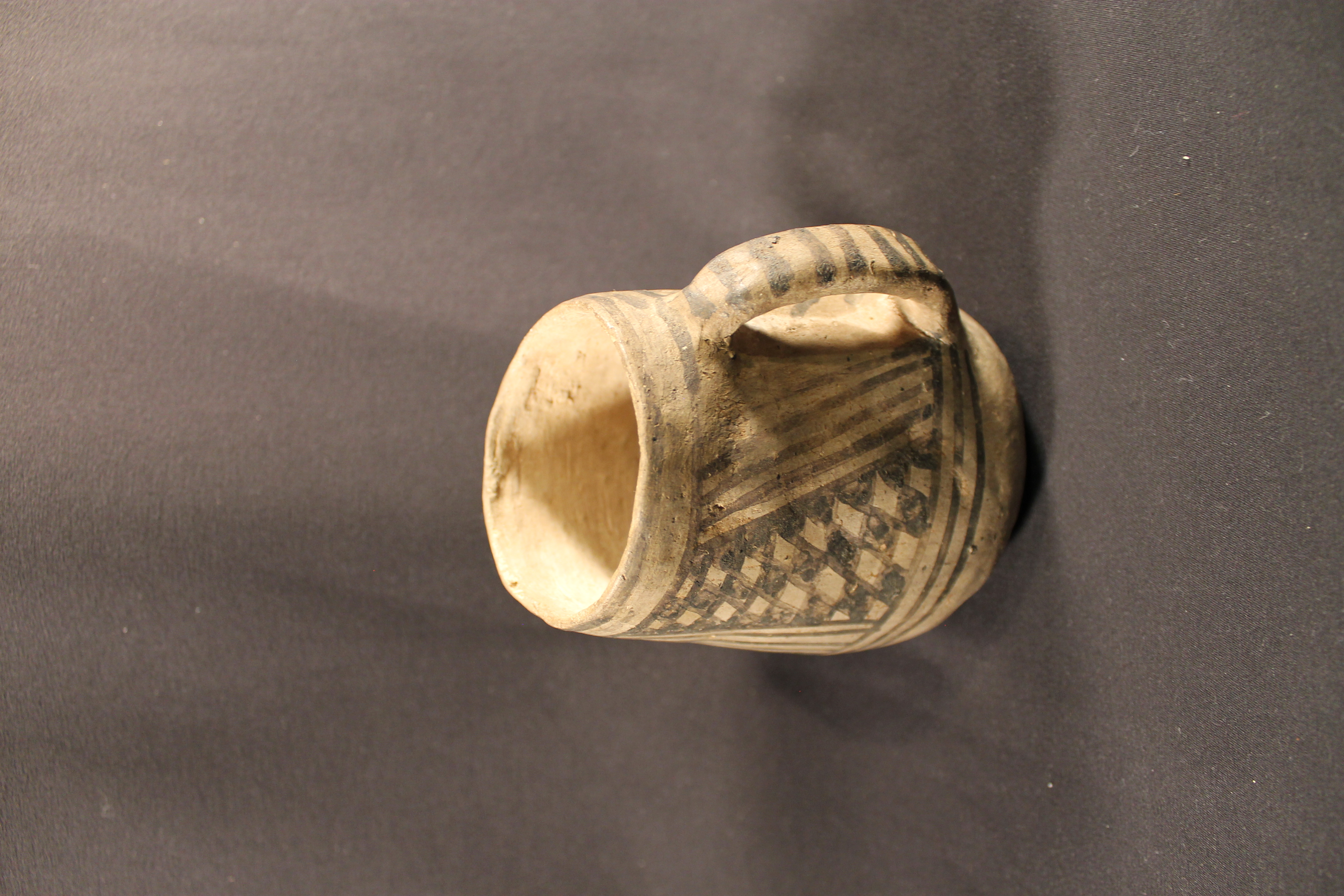 Ceramic handled mug with striped and checkerboard pattern painted in black on surface.