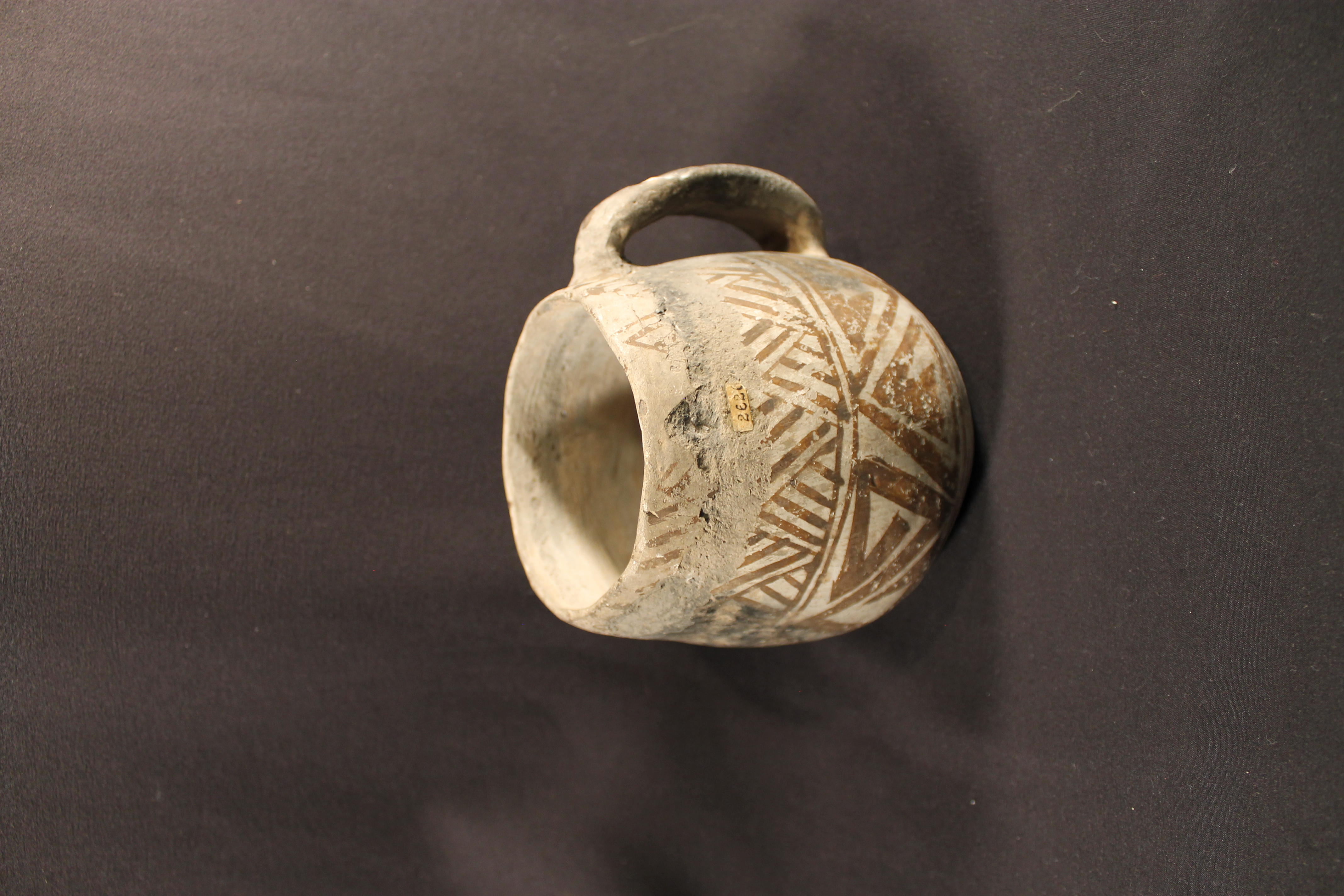 Ceramic handled mug with diamond pattern and perpendicular lines painted in reddish black on the surface.