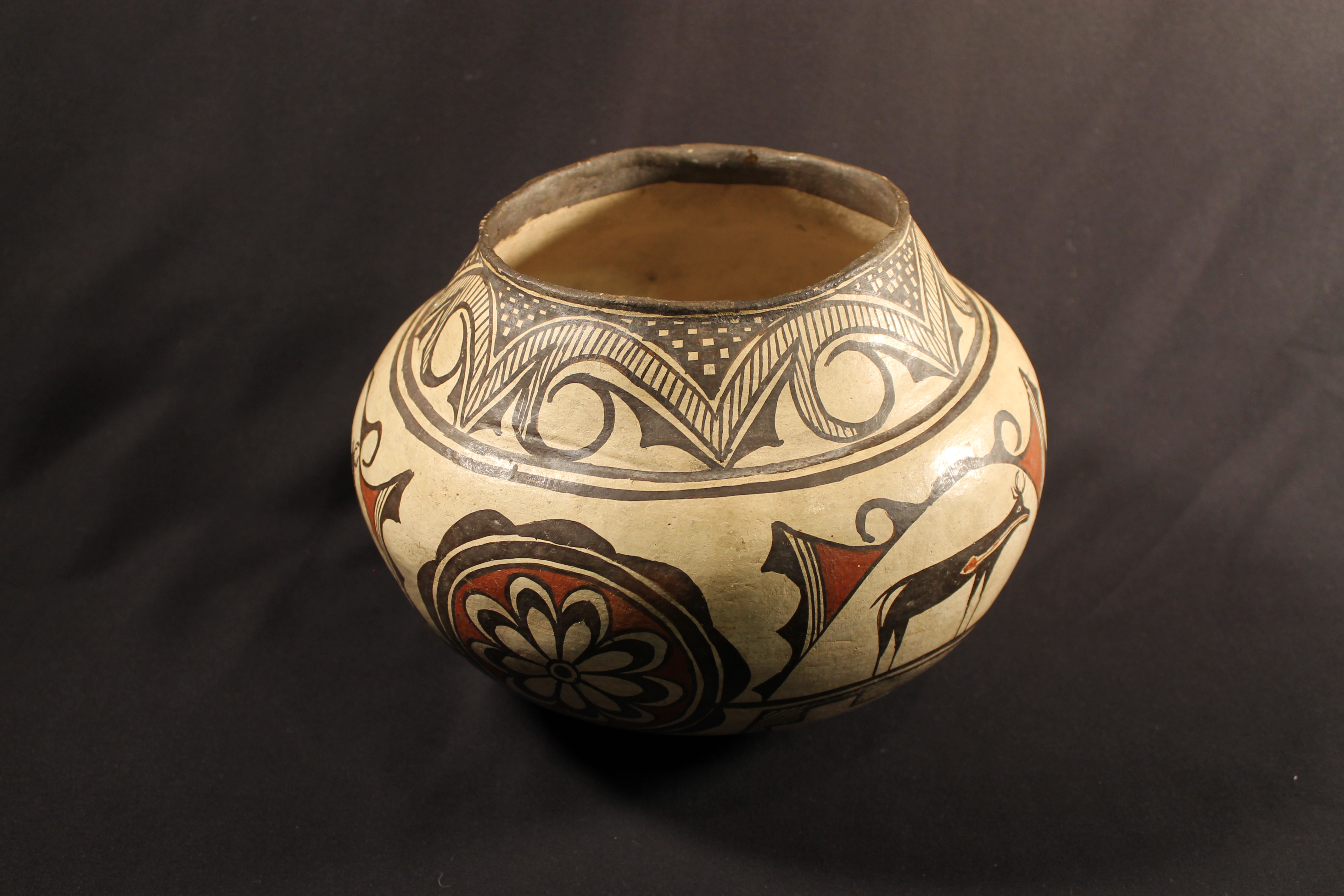 Pottery with red and black design of 3 deer and 3 rosettes on a cream back drop with a break in the upper banding lines