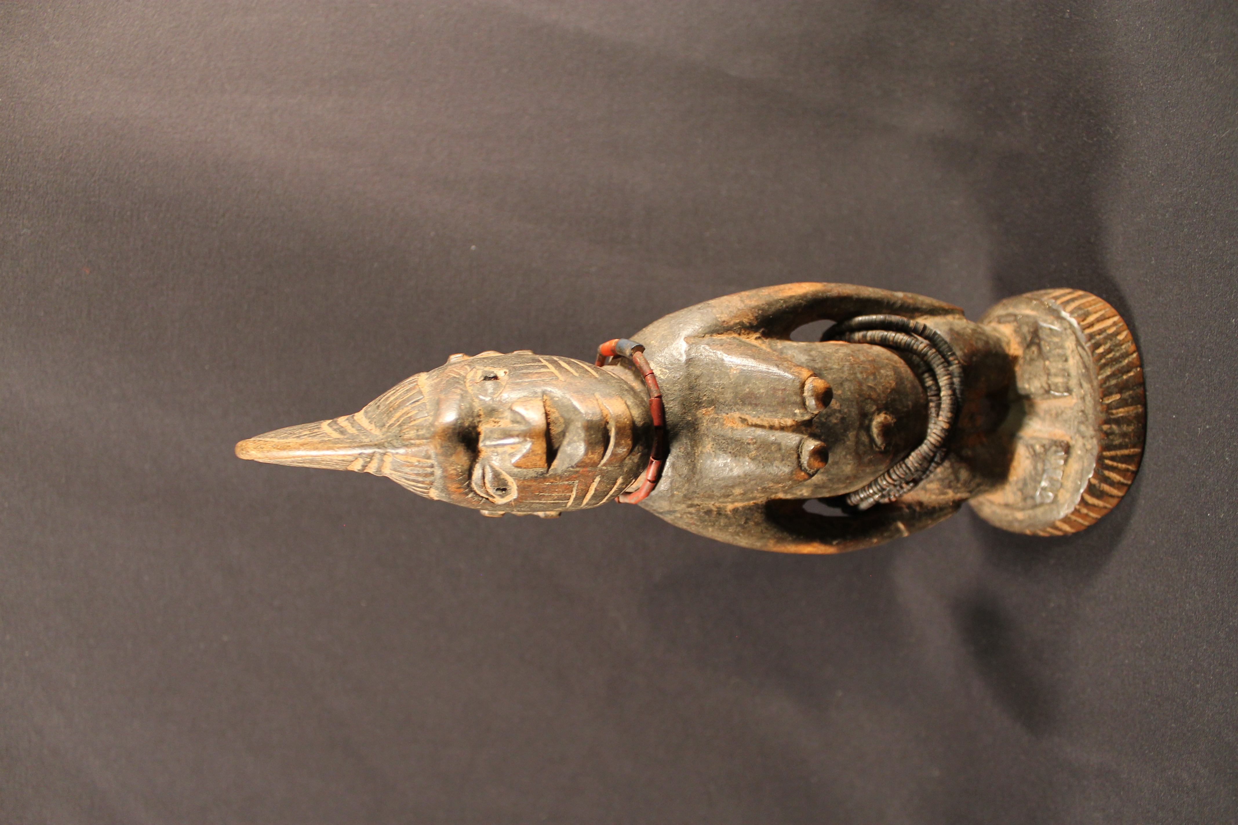 Female figure with crested coiffure, and black and red beads. Figure has evidence of offerings.  