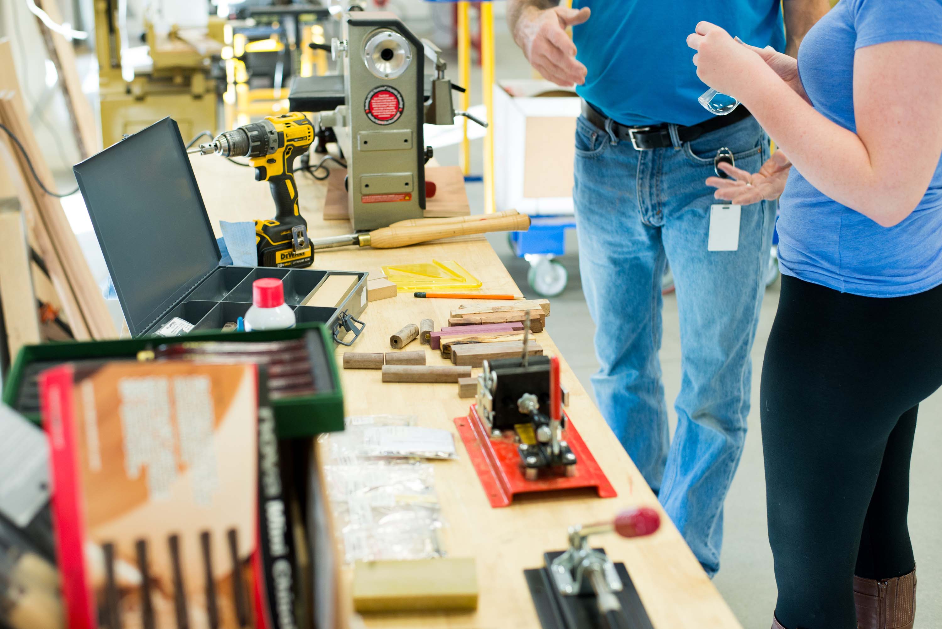 crop image of two people standing next to a table with wood tools and drill bits