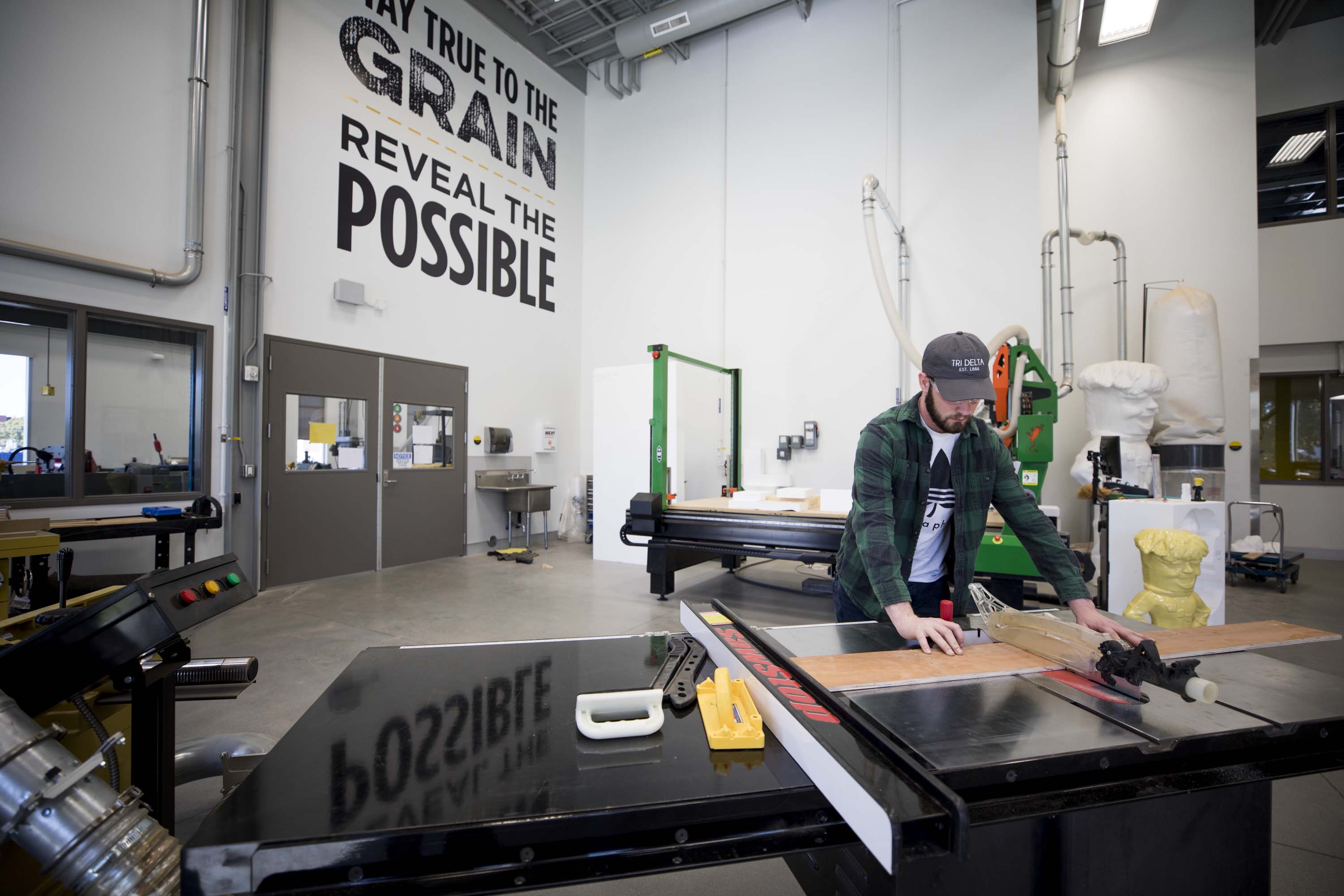 a male cutting wood at table saw in wood lab