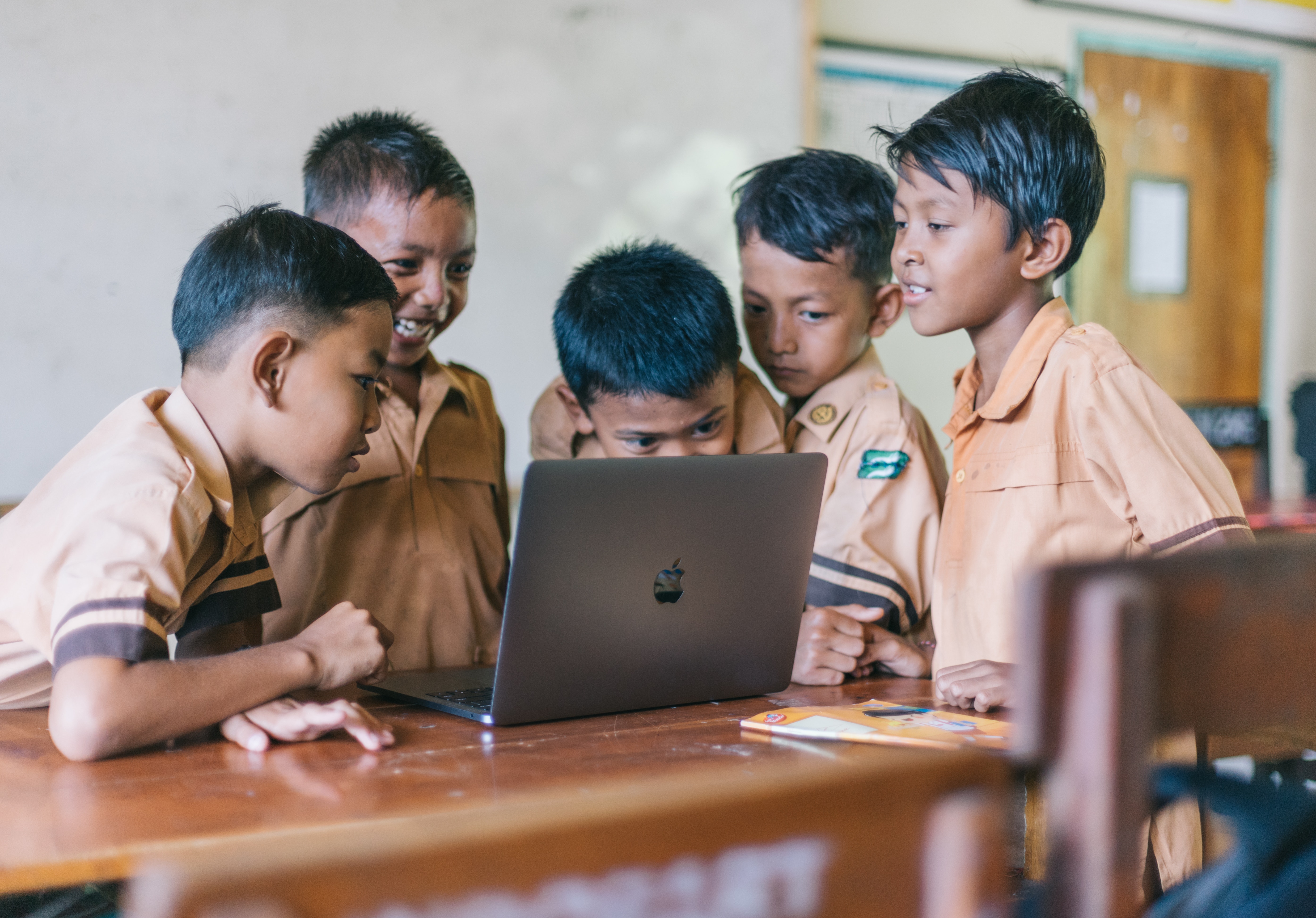 5 refugee schoolboys are curiously looking at a laptop on the desk