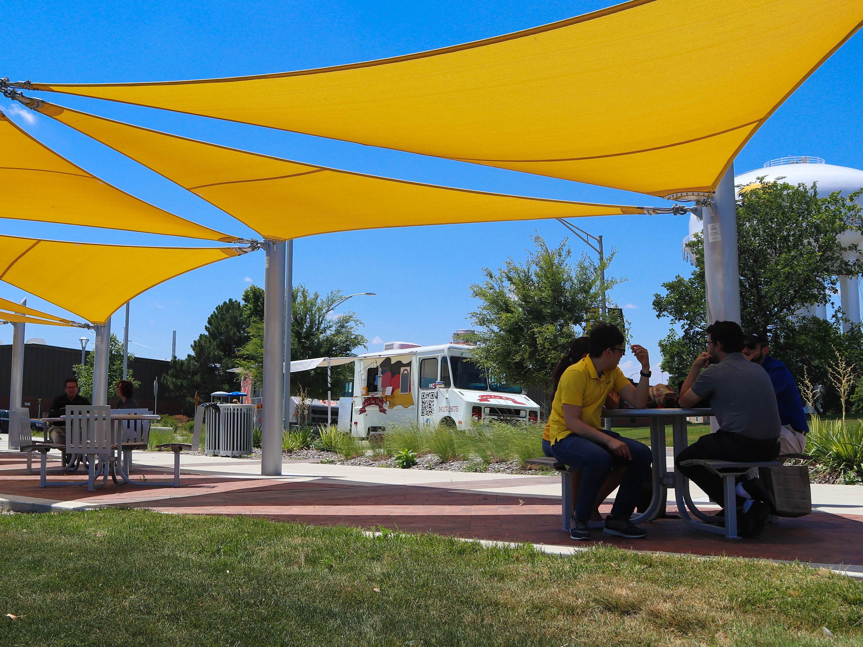 Visitors to the Food Truck Plaza dine underneath the yellow sun shade canopy