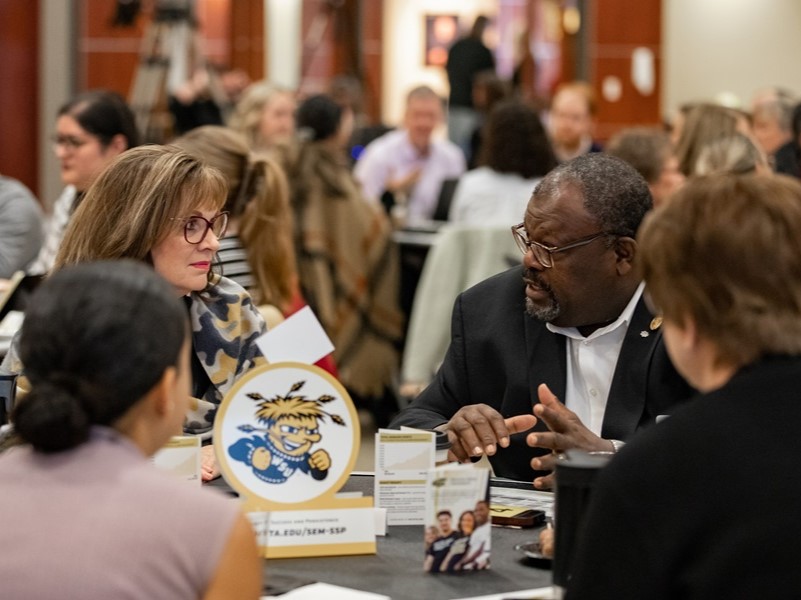 A group of instructors and students having a discussion around a table. 