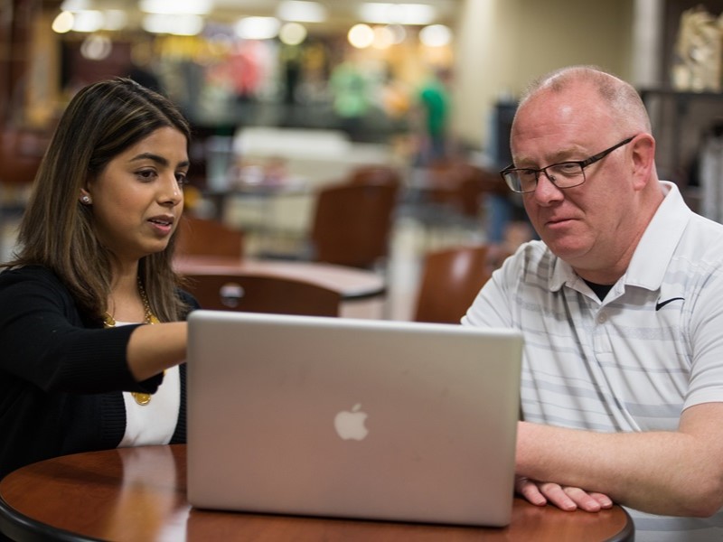 A student assistant going over a subject on a laptop with an adult student. 