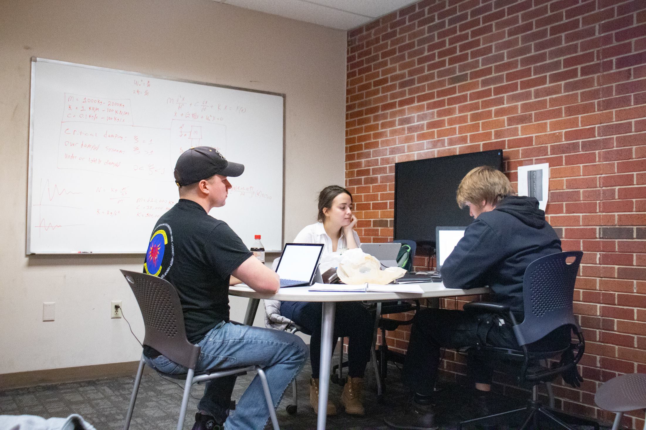 three students studying together at a table with a whiteboard
