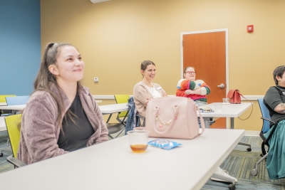 three women smile while watching a presentation